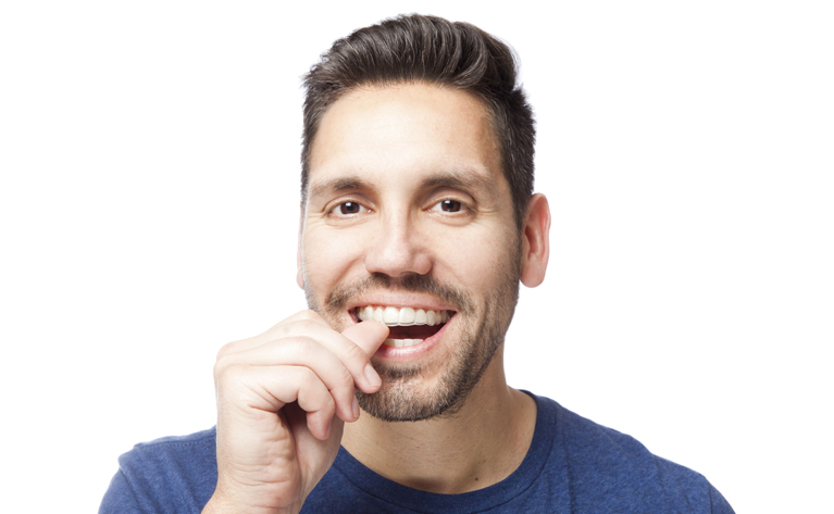 brunette male putting Invisalign clear braces into his mouth at Clapham dental practice