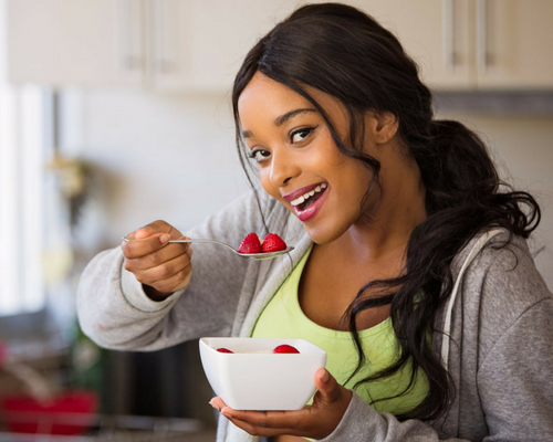 a woman smiling with white teeth in a yellow top eating a bowl of strawberries