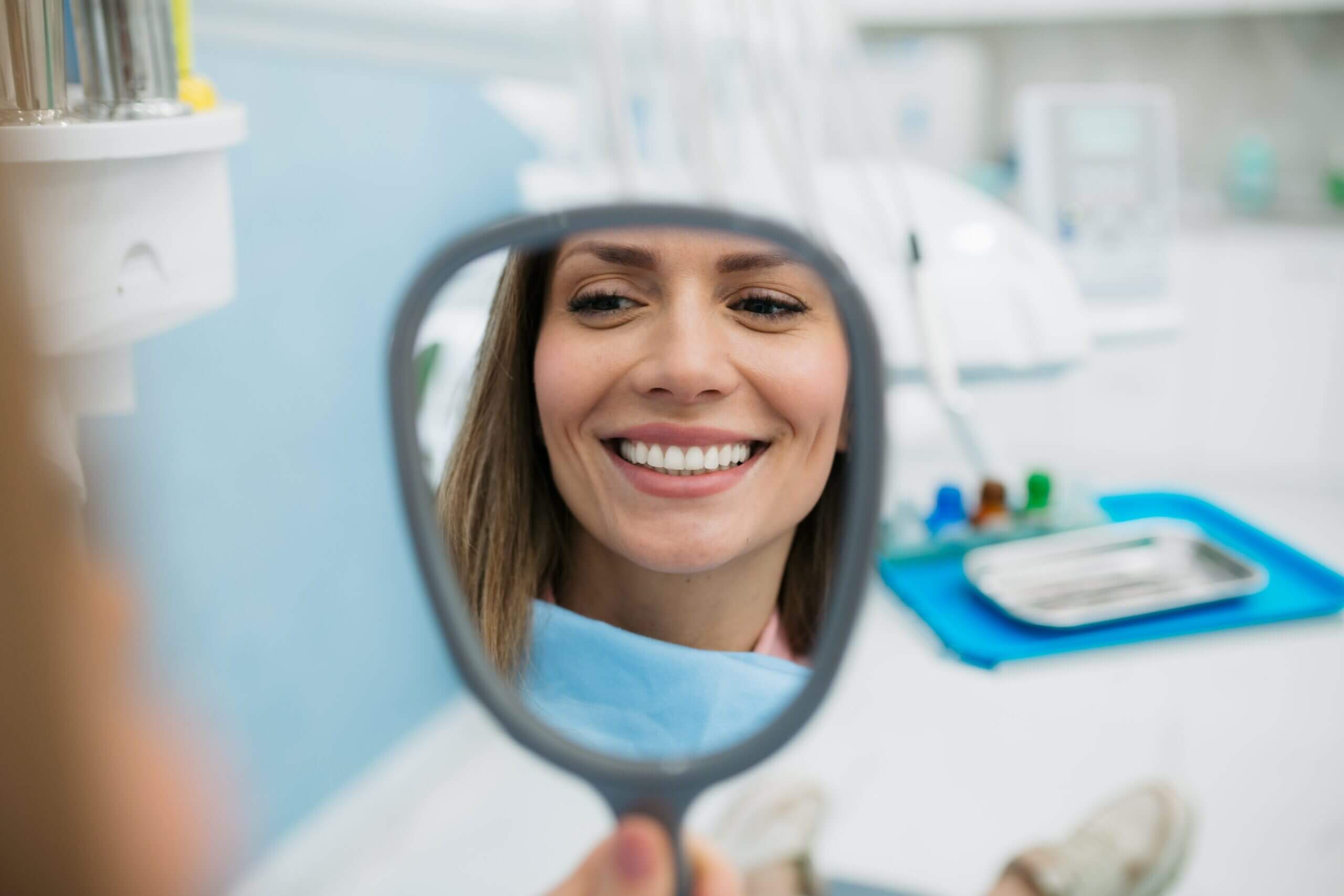 Woman smiling into a mirror at Crescent Lodge Dental Practice, after getting teeth whitening. how dental implants work